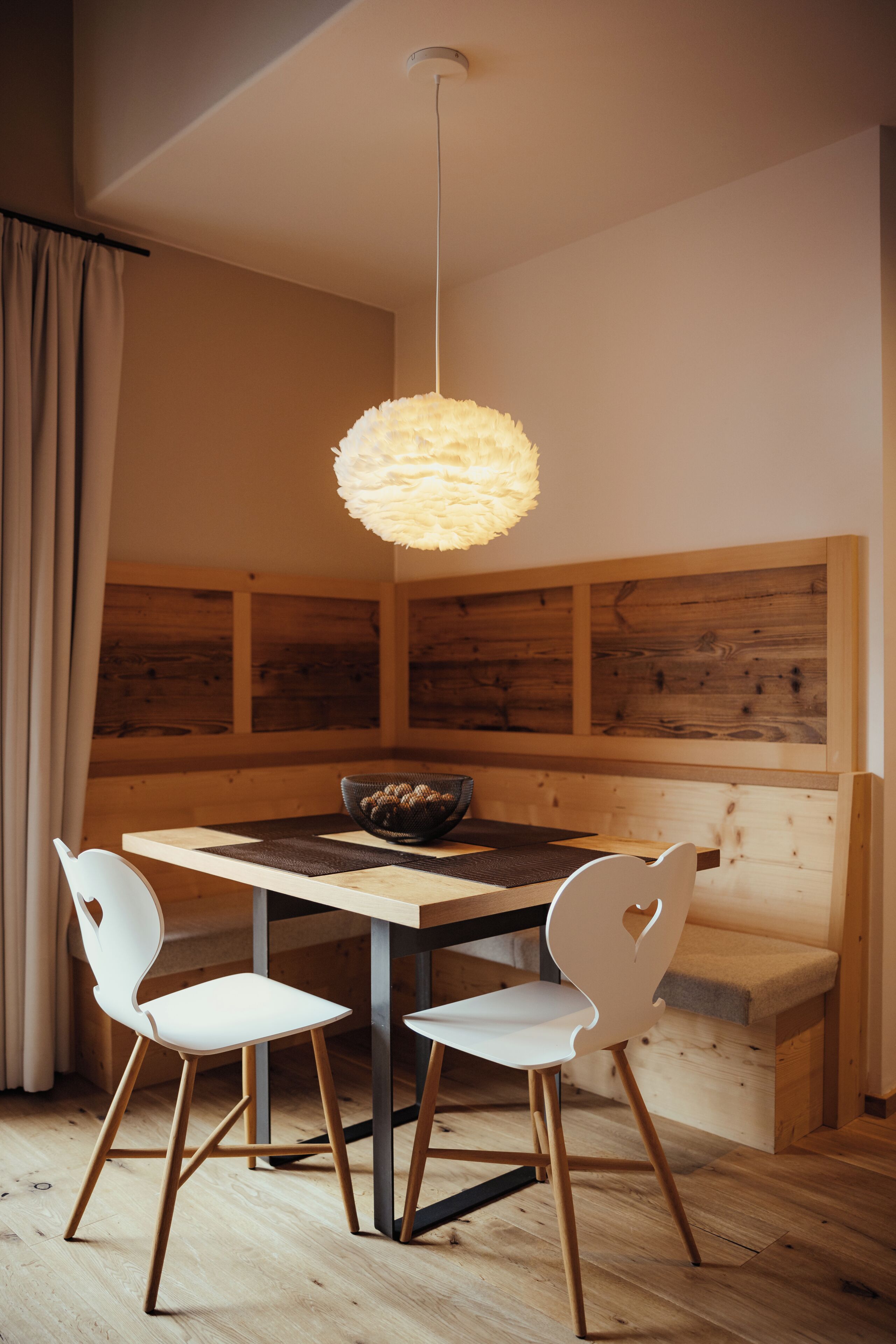 Un comedor con una mesa de madera, sillas blancas, una lámpara colgante y un banco de madera.