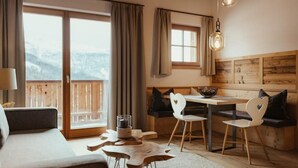A cozy room with a sofa, a dining table with chairs, a bench, and a view of the outdoors. - Villa Flora Mountain Lodges (San Cassiano)