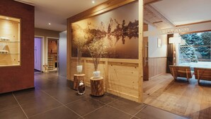 A modern interior with a wooden reception desk, a large wall mural, and a seating area with a view. - Villa Flora Mountain Lodges (San Cassiano)