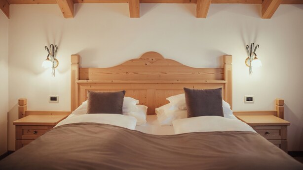 A bedroom with a wooden headboard, two bedside tables, and wall-mounted lamps. - Villa Flora Mountain Lodges (San Cassiano)