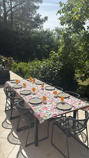 An outdoor dining area with a table set for six, surrounded by chairs, in a garden setting.