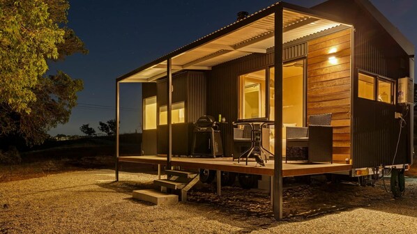 A modern, single-story house with a covered porch, outdoor seating, and a visible grill.
