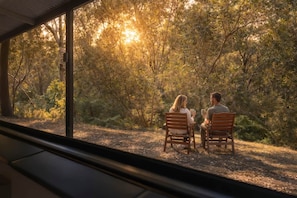 A couple seated on wooden chairs facing a forested area with sunlight filtering through the trees.