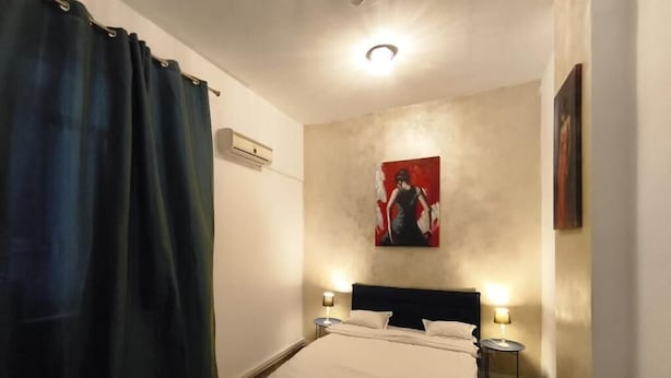 Un dormitorio con una cama, dos mesitas de noche, un aire acondicionado de pared y un cuadro.