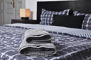 A neatly made bed with a patterned bedspread and pillows, a bedside lamp, and a dark wooden nightstand.