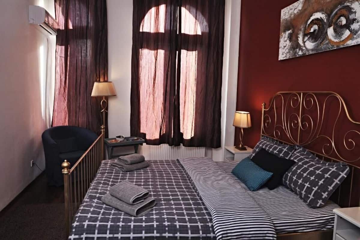 Quarto de hotel com uma cama, duas mesas de cabeceira, uma cadeira, uma janela com cortinas e um quadro na parede.