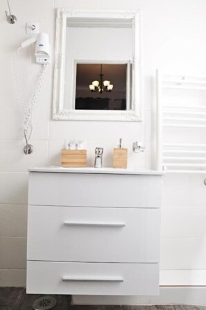 A white bathroom with a mirror, a hairdryer, and a wooden box on the vanity.