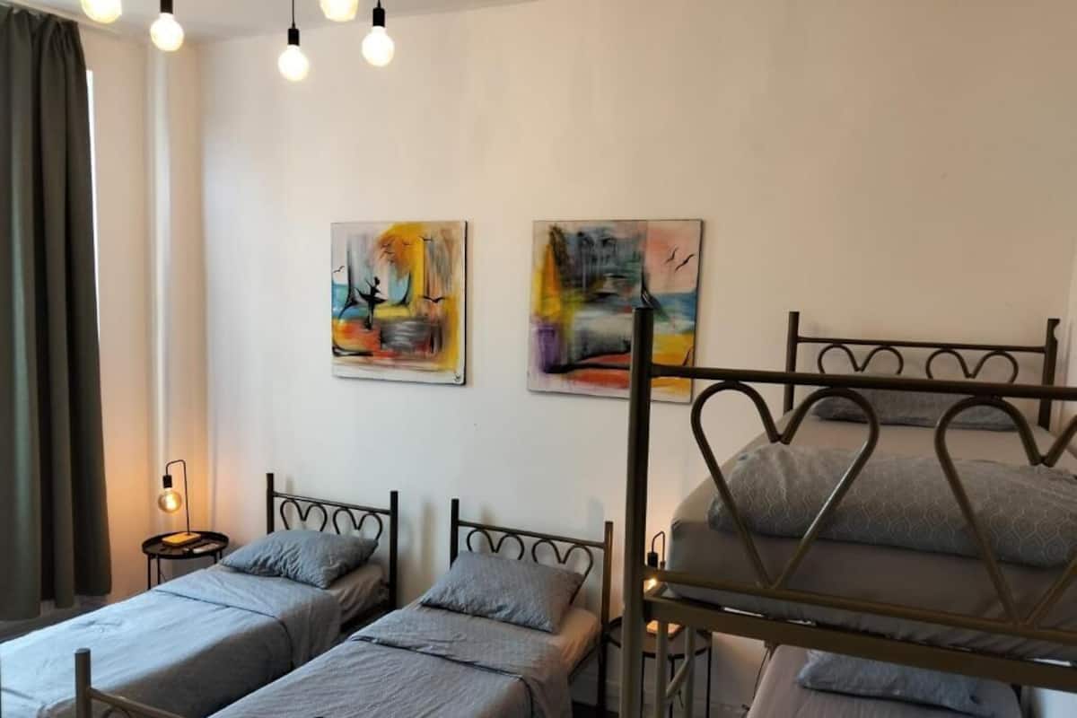 Quarto com duas camas individuais, uma beliche e duas pinturas abstratas na parede.