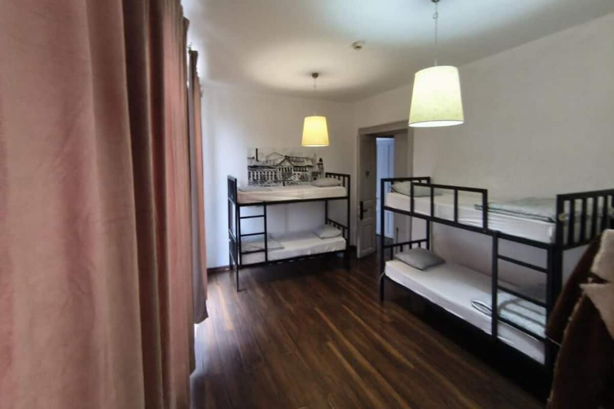 Quarto com beliches, piso de madeira, uma porta e luminária pendente.