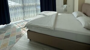 Une chambre avec un grand lit, une armoire et une vue dégagée à travers des rideaux légers.