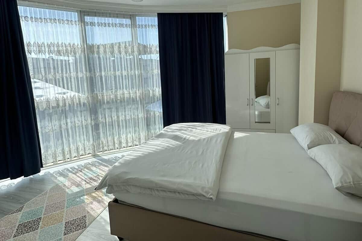 Une chambre avec un grand lit, une armoire et une vue dégagée à travers des rideaux légers.