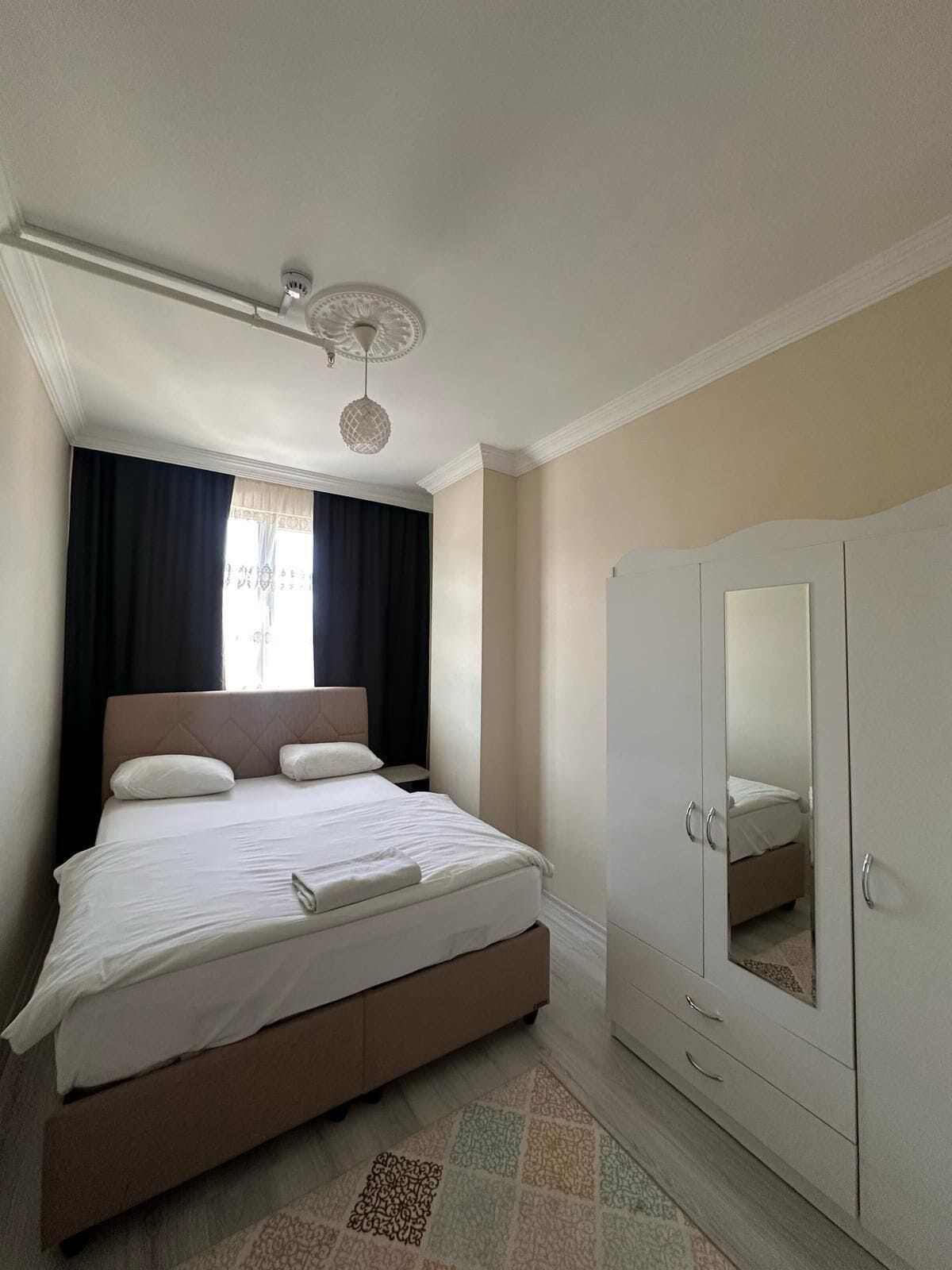A bedroom with a bed, a wardrobe, a ceiling light fixture, and a window with curtains.