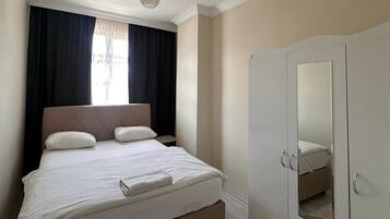 A bedroom with a bed, a wardrobe, a ceiling light fixture, and a window with curtains.
