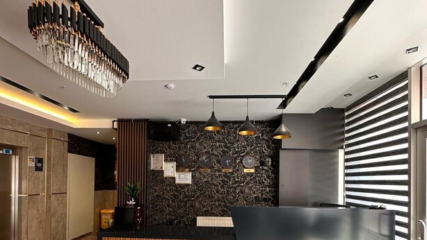 Un espace d’accueil moderne avec un sol en marbre, une moquette rouge, un comptoir d’accueil en bois, un mur noir orné d’horloges et un luminaire suspendu.