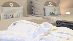 Una cama bien hecha con sábanas blancas y un albornoz doblado encima.