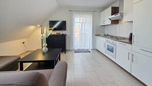 Una cocina moderna con armarios blancos, horno empotrado y microondas. Hay una mesa de comedor con un florero y un sofá en la sala de estar.
