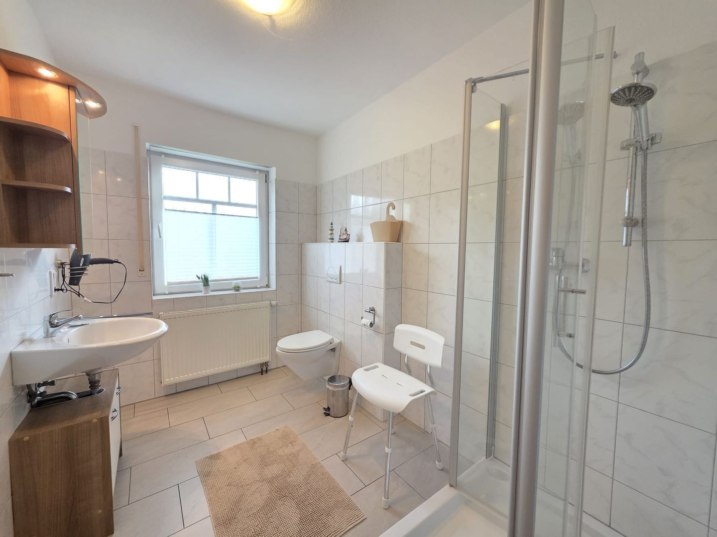 Un baño moderno con ducha envuelta en vidrio, un lavamanos blanco, un inodoro y una ventana que proporciona luz natural.
