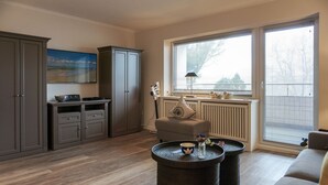 Una sala de estar moderna con un sofá, dos mesitas redondas, un mueble aparador y un ventanal con persianas.