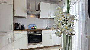 Een moderne keuken met witte kasten, een inbouwoven en een vaas met witte bloemen op het aanrecht.