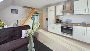 Een modern appartement met een woonruimte, inclusief een bank en een vaas bloemen, een keuken met witte kastjes en een fornuis, en een houten trap.