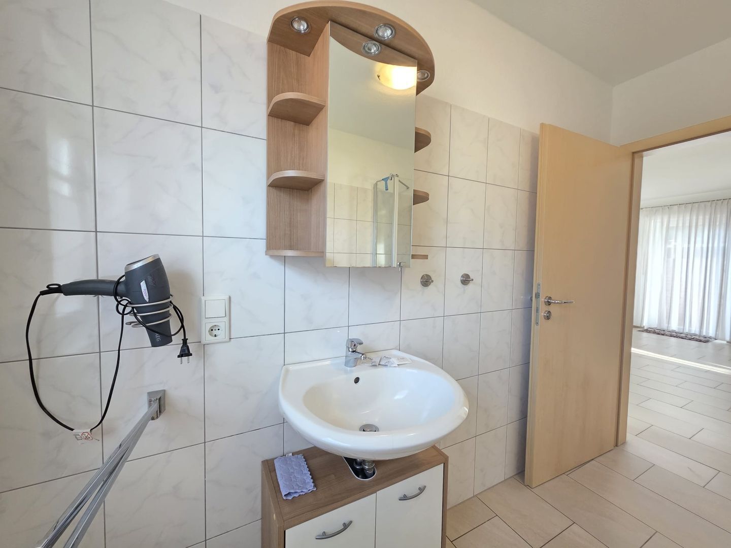 Un baño con un lavamanos blanco, un secador de pelo, un espejo y un armario de madera.