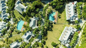 Vue aérienne d’un complexe hôtelier comprenant plusieurs bâtiments, une piscine et des palmiers.