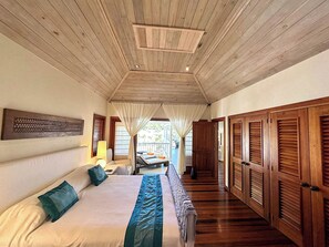 A spacious bedroom with a large bed, wooden ceiling, and a view of the outdoor area.