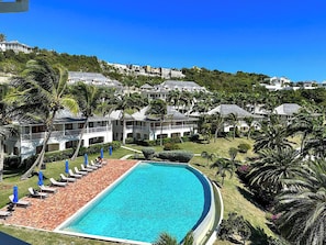 A resort with a large swimming pool, sun loungers, and a view of the surrounding hillside.