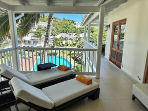 A balcony with two sun loungers, a small table, and a view of a swimming pool and surrounding greenery.
