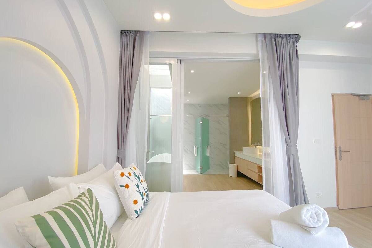 A modern hotel room with a large bed, a bathroom with a glass shower, and a view of the city.