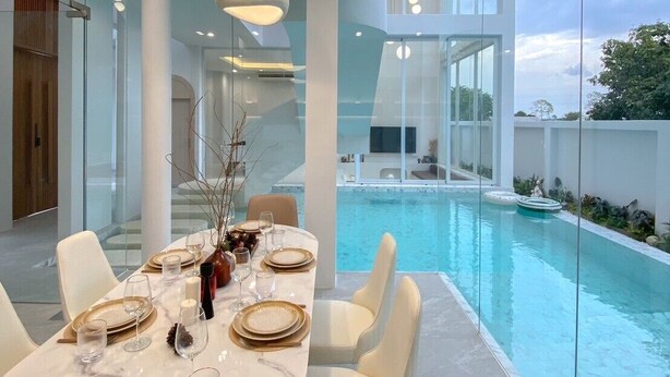 A modern dining area with a pool view, featuring a marble table, white chairs, and pendant lighting. - The Pool Space — ICONIC Pool Villa (Pattaya)