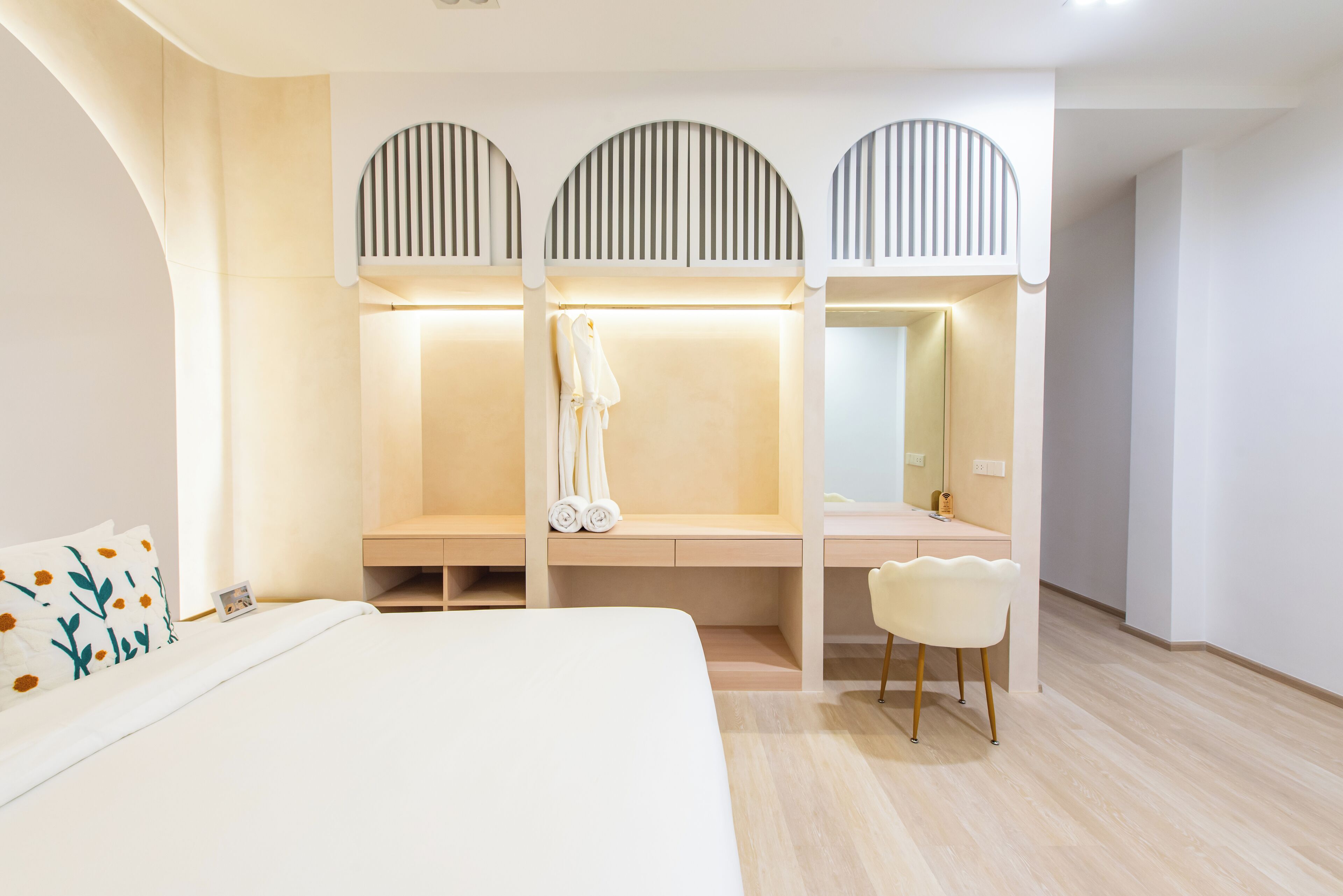 A modern hotel room with a large bed, a vanity with a mirror, and a seating area with a chair.