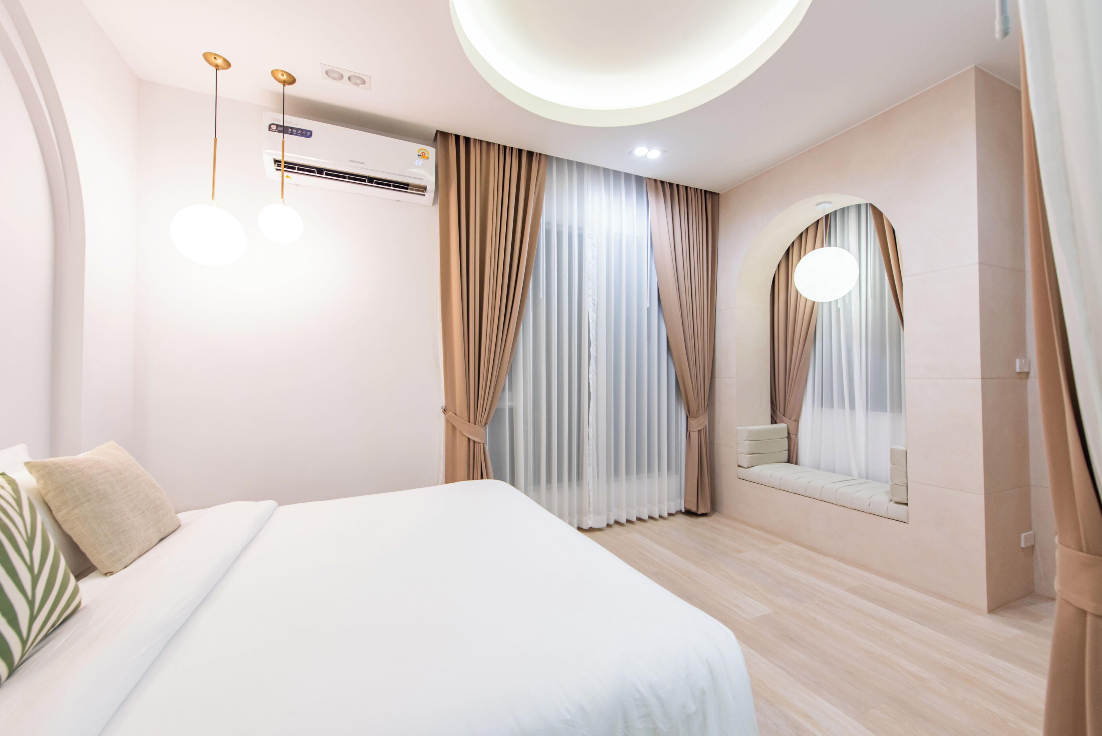 Un dormitorio moderno con una cama grande, un banco empotrado, aire acondicionado de pared y una lámpara en el techo.