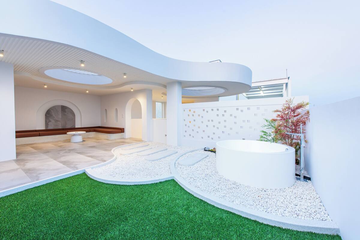A modern spa area with a circular hot tub, a small seating area, and a pathway leading to a door.