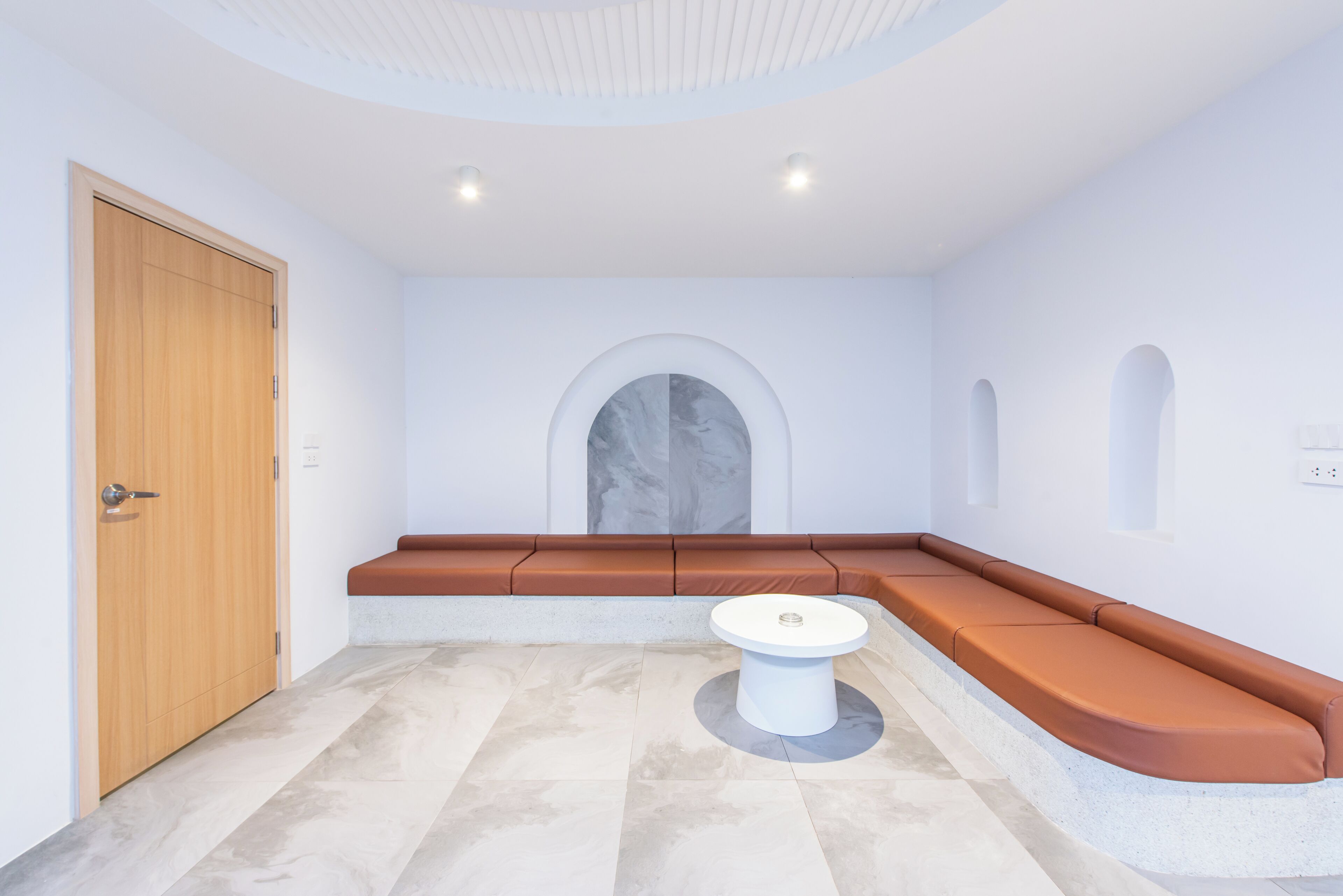 A modern room with a wooden door, a round white table, and a curved seating area with orange cushions.