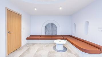 A modern room with a wooden door, a round white table, and a curved seating area with orange cushions.