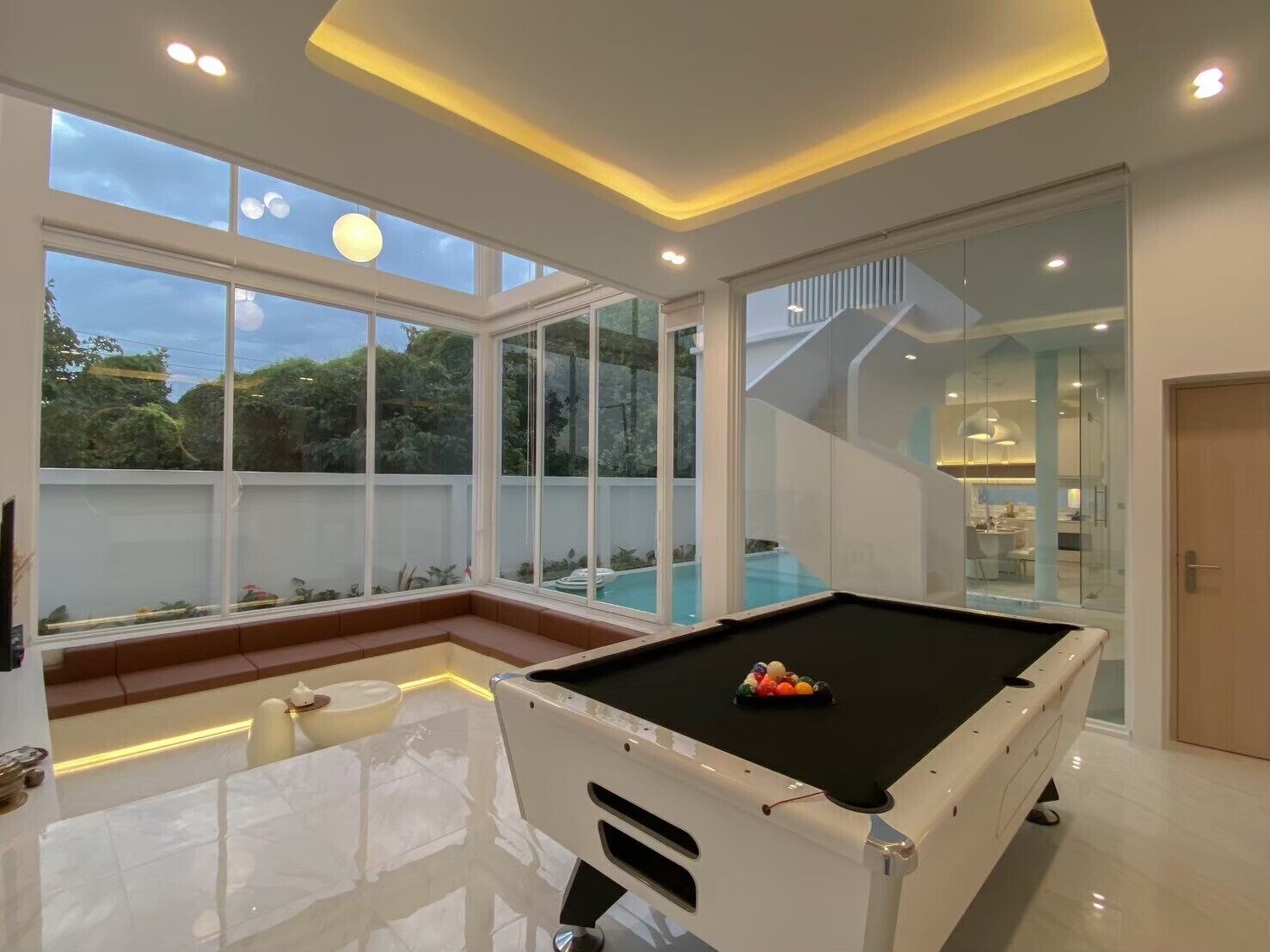 A modern indoor pool area with a pool table, large windows, and a staircase leading to an upper level.