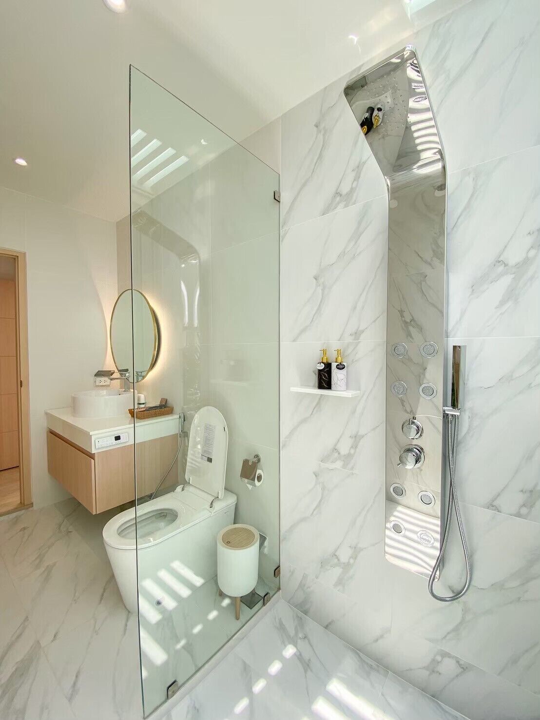Une salle de bain moderne avec une douche en verre, des toilettes, un lavabo avec un miroir et des murs en marbre.