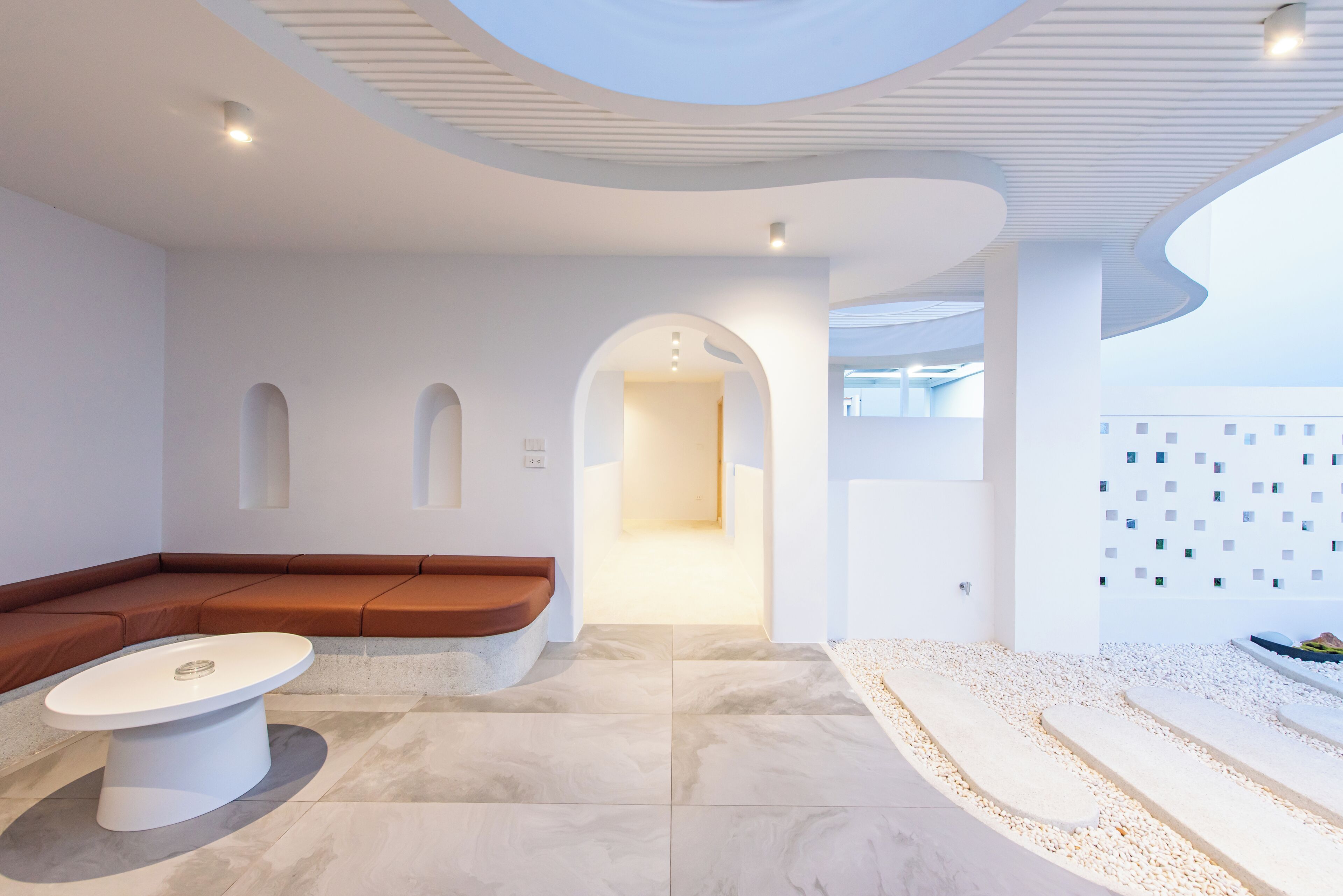 A modern interior with a curved ceiling, a seating area with a brown bench, a white table, and a tiled floor.