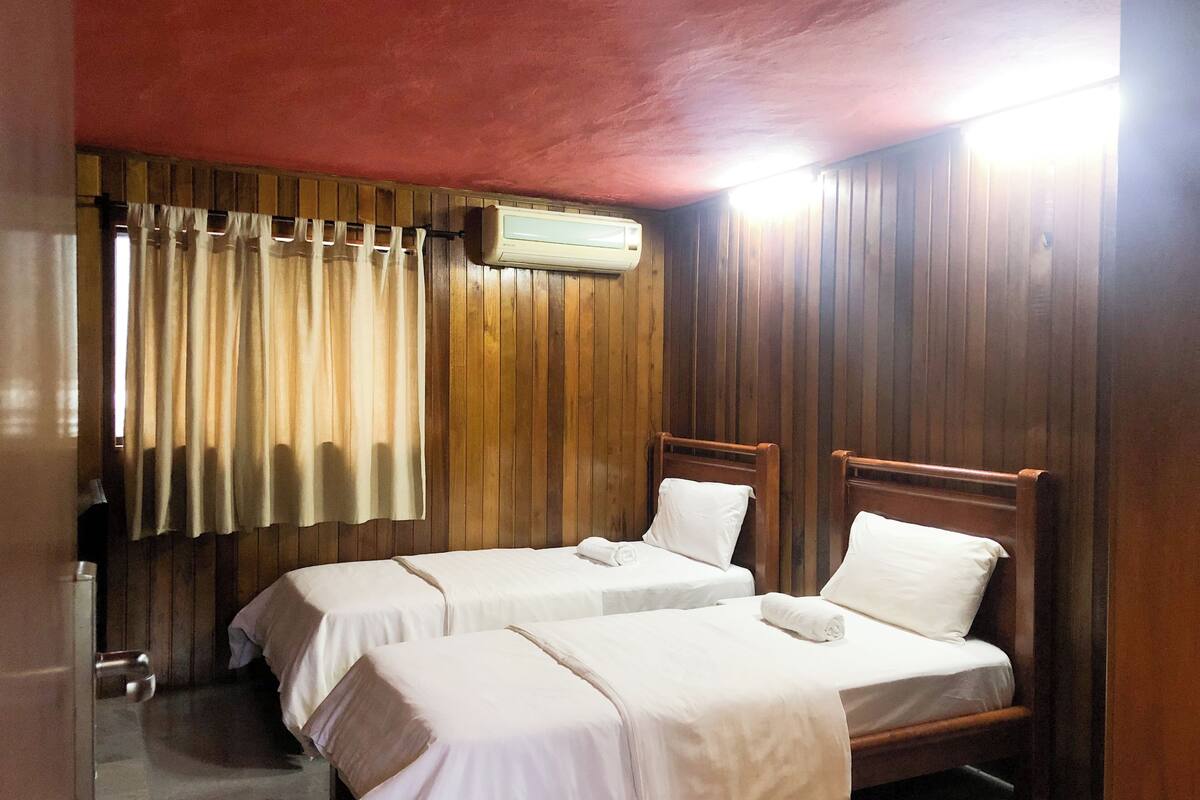 Une chambre avec deux lits en bois, une fenêtre avec des rideaux et un appareil de climatisation.