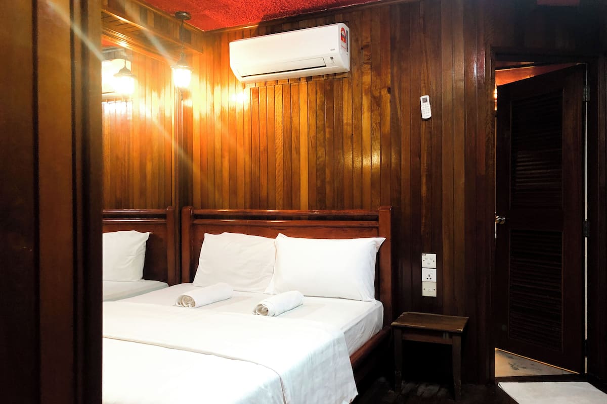 Une chambre d’hôtel avec des boiseries, un lit recouvert de draps blancs, un appareil de climatisation et une petite table de chevet.