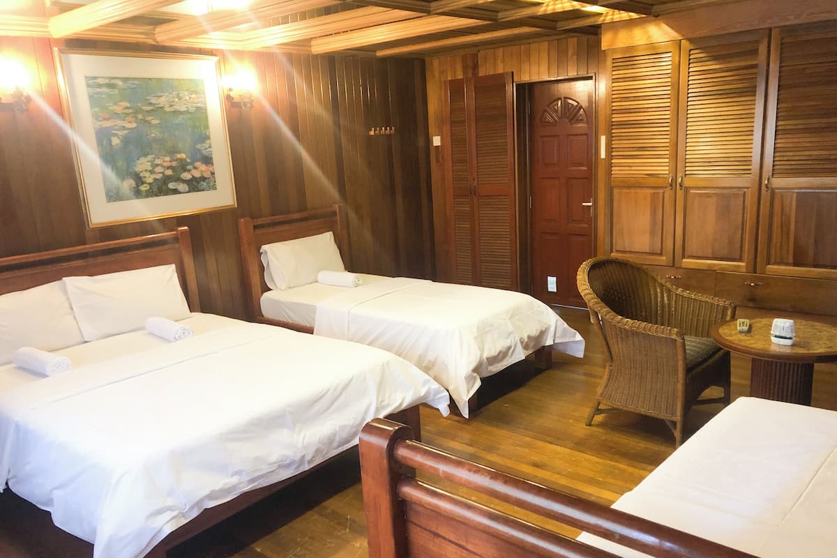 Une chambre d’hôtel avec deux lits, un plafond en bois, une chaise en osier et une petite table.