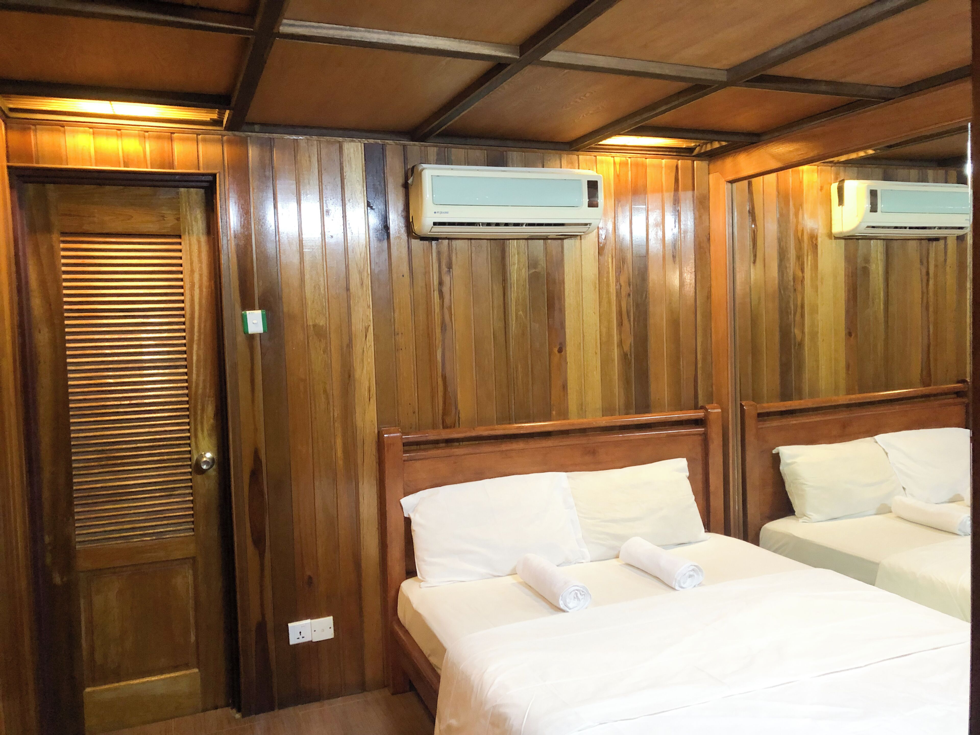A hotel room with wooden paneling, two beds with white linens, and two wall-mounted air conditioning units.