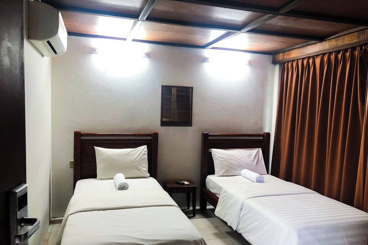 Une chambre d’hôtel avec deux lits simples, une petite table, une table de chevet et un ventilateur de plafond.
