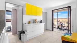 Una cocina moderna con armarios blancos, un mueble superior amarillo y un balcón con mesa y sillas.