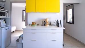 Una cocina moderna con armarios blancos, un armario superior amarillo, una cafetera y un microondas.