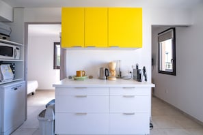 Une cuisine moderne avec des meubles blancs, un meuble supérieur jaune, une machine à café et un four à micro-ondes.
