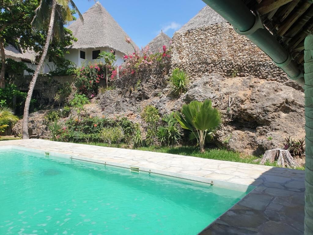 Una piscina dalle acque cristalline, circondata da vegetazione tropicale e strutture in pietra.