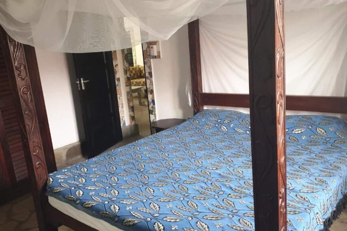Una cama con dosel de madera adornada con un dosel blanco y un edredón azul.