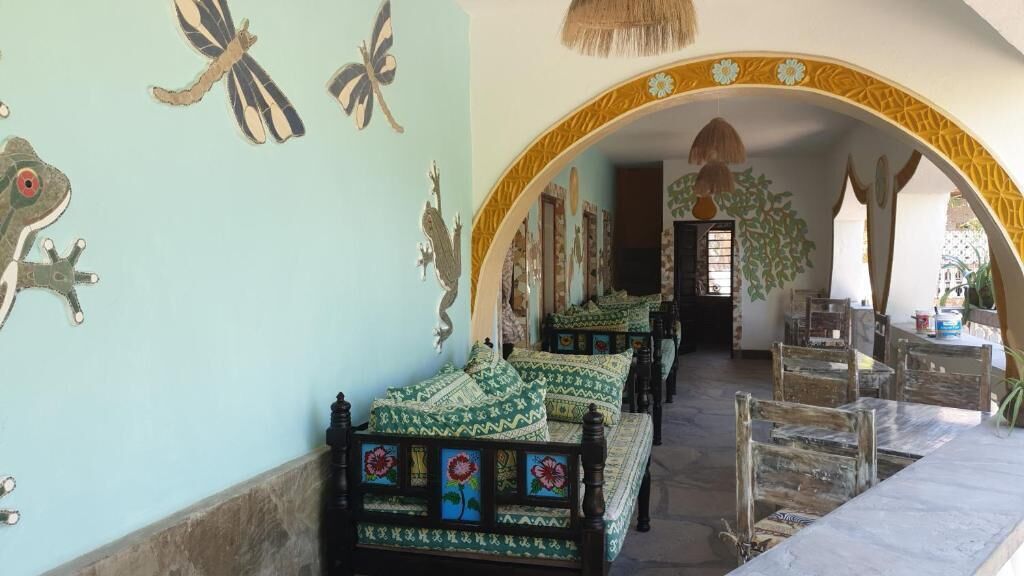 A room with a long corridor, a bed with patterned bedding, and a wall decorated with frog and butterfly motifs.